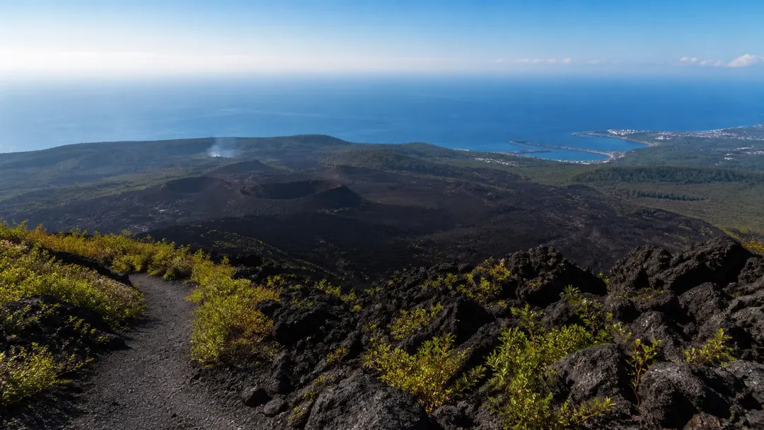生成AIイメージ画像: 伊豆大島の火山地形を車なしで巡る2泊3日モデルコース。人物なしで、黒い火山地形と緑の低木、海と港を一続きに表現