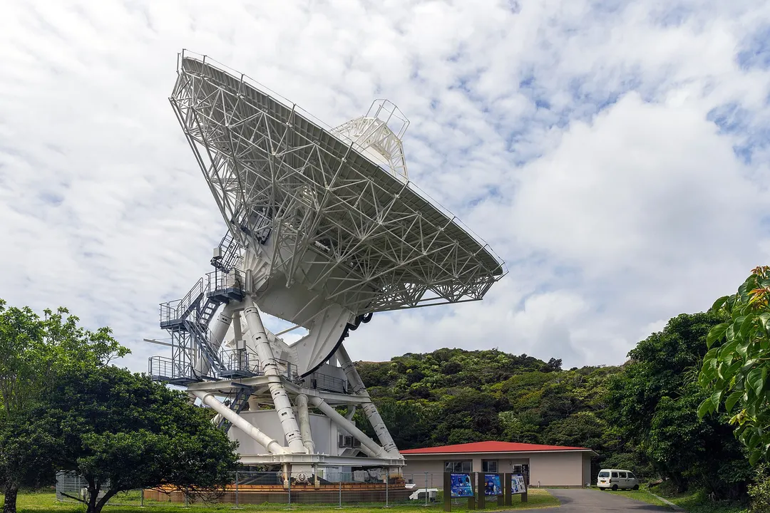 森を背に立つVERA小笠原観測局の20m電波望遠鏡の全景。昼間の外観写真です。
