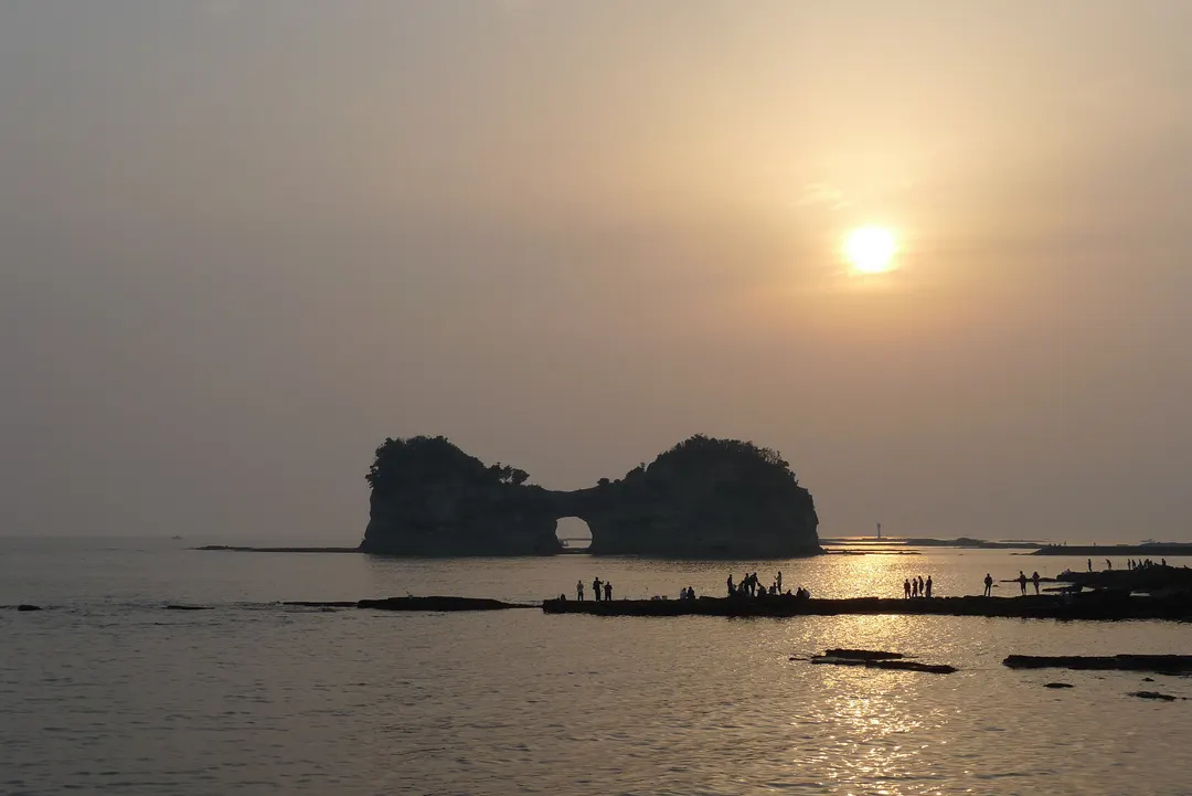 夕日を背にした円月島と白浜の海岸を写した実写写真