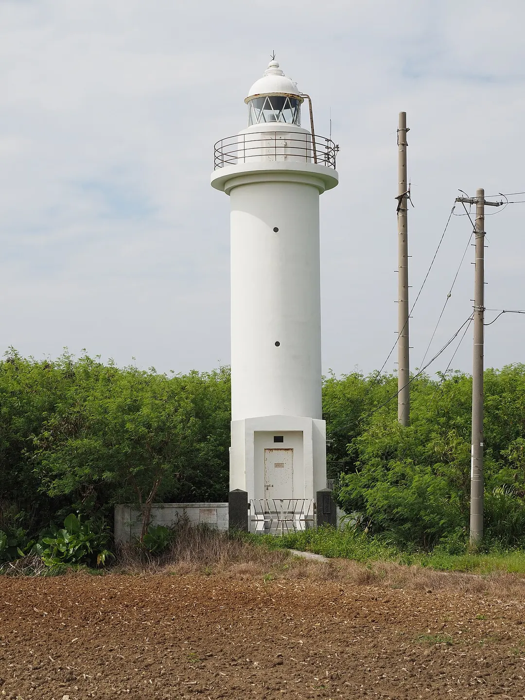 波照間島の畑と亜熱帯の植生の中に立つ白い波照間島灯台を写した実写写真
