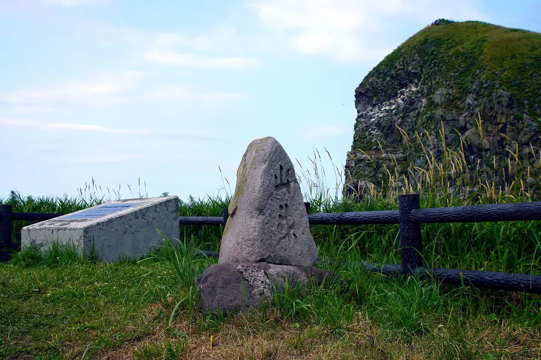 利尻島のペシ岬にある会津藩士の墓碑と岬の岩山を写した実写写真