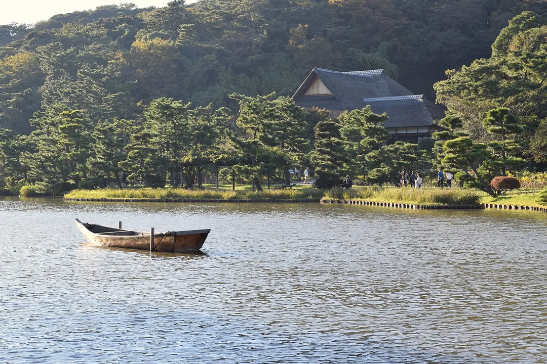 三溪園の大池と岸辺の園路、木々の間に見える屋根